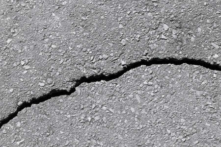 Asphalt track with a crack in a broken line. Asphalt grey color with small pebbles and gravel. A deep crack in the road.の写真素材