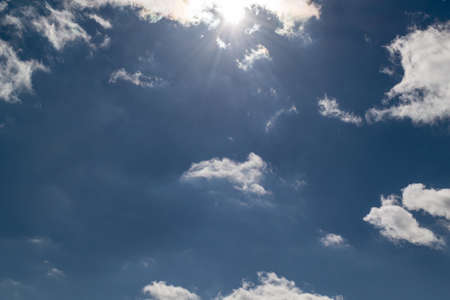 Beautiful deep blue sky with white Cumulus clouds. At the top the sun shines. From the sun in different directions the rays of the sun. Present and Cirrus clouds.の写真素材