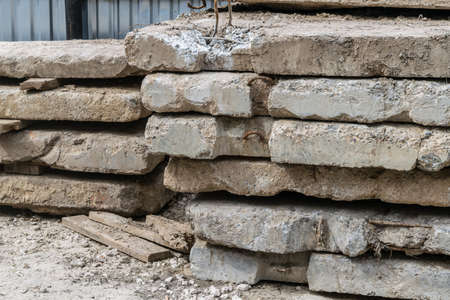 On the ground lies a stack of old concrete slabs. Plates are laid on wooden boards. The plates have cracks and cracks. In the background a fence made of metal profile.の写真素材