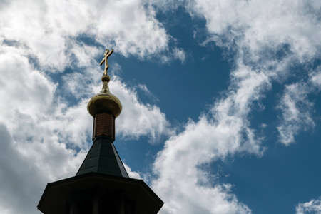 The Golden dome of the Church with a cross on the sky background with white clouds. Visible wooden tower covered with a metal roof.の写真素材