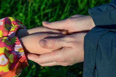 Mother holds the hand of his daughter. She warms his hands. They trust each other. Adult cares about the child.の写真素材