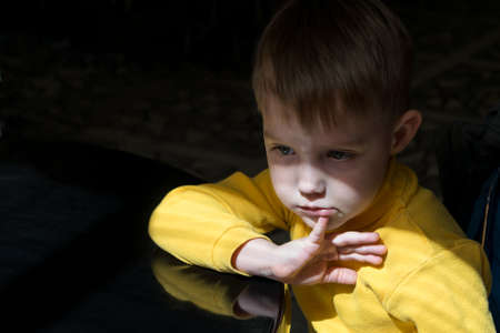 Little boy sitting at the table in a pensive state. The boy backs her fingers to her lower lip. He...