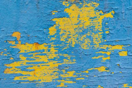 Wooden surface painted with paint in several layers. Paint cracked and peeled off in some places. Paint color blue and yellow. There are streaks and spots of red paint.の写真素材