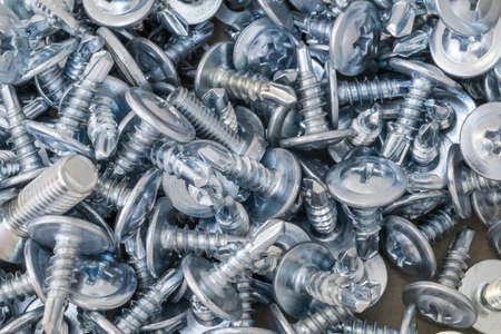 A bunch of screws lying on the table. There are a few screws. The head of the screws under the Phillips-head screwdriver. They are new, shiny, zinced.の写真素材