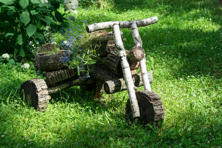 In the forest in the clearing stands a motorcycle from wooden logs. A motorcycle with a sidecar or bassinet. The carrycot and seat are baskets with flowers.の写真素材