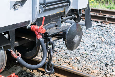 Drawbar railway car with an air hose and chain. Rails with concrete sleepers. In the background the rails and gravel. Convex coupling circle. Rail car gray. Day, the sun is shining.の写真素材