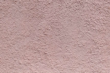 The rough texture of the decorative plaster on the wall. The surface of pink or beige with drips, drops and cracks. There are dimples and bumps.の写真素材