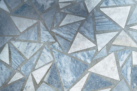 Floor or surface lined with marble slabs of triangular form. Triangular marble tiles and light gray or beige with stripes, lines and spots. Joints filled with cement or concrete.の写真素材