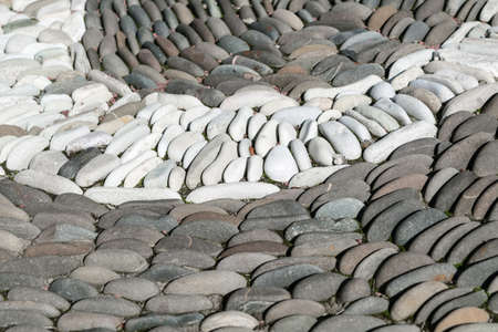 White oval stones stacked arch or semi-circle among the dark stones. The stones are located one behind the other in several rows. Between the stones are small leaves.の写真素材