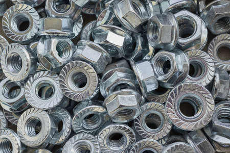 A bunch of shiny new metal hex nuts lying chaotically. Nuts with a round base with notches. Nuts clean. Scattered by different parties. Abstract background.の写真素材