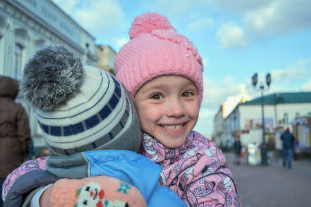 A girl with brown eyes hugs her brother and smiling with happiness showing on her faceの写真素材