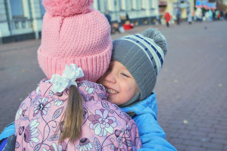 The boy hugs the girl and smiles and is happy. Brother hugging sister loves her. On the face emotions and feelings. Pulls her to him. The boy's blue eyes. They make friends and walk on the street.の写真素材