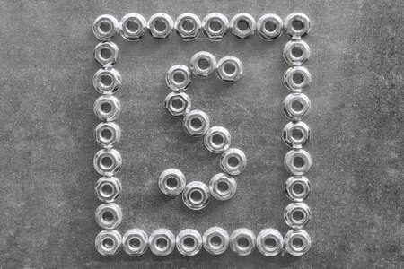 The letter s of the English or Latin alphabet lined with metal nuts. Around the letter's frame of shiny new nuts. The nut and the letter s lying on a metal chrome-plated Board.の写真素材