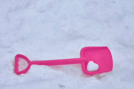 The white snow lies a children's shovel. The shovel is the snow in the shape of a heart. The heart a symbol of love and Valentine's day holiday. Shovel plastic pink. Outdoors day, is pure white snow.の写真素材
