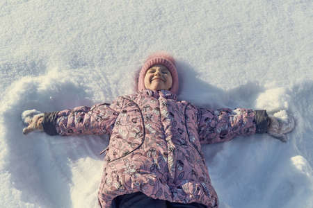 Girl lying on her back in the snow, hand in hand. The girl narrowed her eyes and wrinkled my nose and smiles. She was pleased and happy. Tracks in the snow from his hands like the wings of an angel.の写真素材