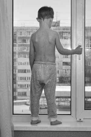 Little boy stands on the sill of the window.の写真素材
