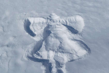 On the white snow the imprint of a child in the form of an angel flapping its wings. Angel's visible head, wings, dress, leg. Rrelief print. Sunny day. Pure snow. Winter vacation on vacation, holidaysの写真素材