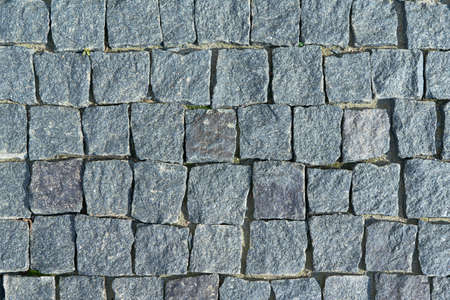 The pavement laid with square stone cobbles of granite. Rough stones, rough. The shape of the stones is uneven and square. Color dark gray. Background, texture or backdrop.の写真素材