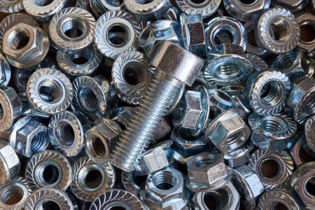 Shiny metal bolt lying on a pile of scattered nuts. Abstract background for industry from the new shiny nuts. Bolt and nuts for fixing. Chaos and confusion from the nuts.の写真素材