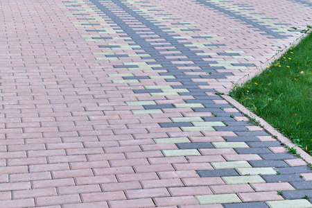 The sidewalk is lined with stone blocks of rectangular shape. On the right side of the lawn with green grass. On the edge of the paving border. Tiles are laid with a pattern.の写真素材