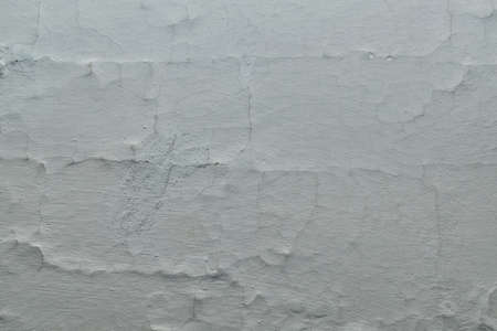 The surface of the old furnace wall painted with white paint. The surface is cracked by vertical and horizontal cracks. The paint swelled. Points, bumps and hollows. Background, texture, backdrop.の写真素材