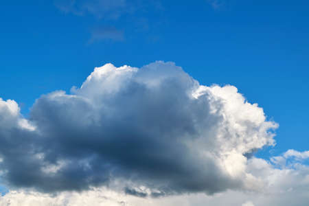 A large dark Cumulus cloud obscures the clear blue sky. Clouds before rain. Background, backdrop, Wallpaper. Pre-storm weather. Sunlight illuminates a huge cloud.の写真素材