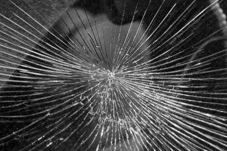 Cracks from the impact on the windshield of the car. The cracks radiate from the center of the impact. Collision with flying stones on the road. Risk and danger of damage. Robbery or vandalism.の写真素材
