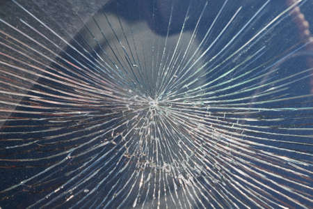 Cracks from the impact on the windshield of the car. The cracks radiate from the center of the impact. Collision with flying stones on the road. Risk and danger of damage. Robbery or vandalism.の写真素材