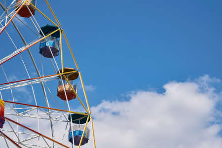 A large Ferris wheel at an amusement Park on a background of blue sky. Several cabins with roofs in the form of umbrellas. The sturdy construction is decorated with colorful bulbs.の写真素材