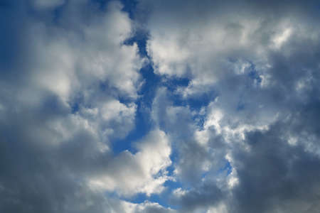 Rain clouds creep on both sides and cover the clear blue sky. There's a gap in the middle between the Cumulus clouds. Weather forecast and meteorology. Background, backdrop.の写真素材