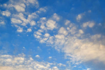 In the blue sky with many little white clouds lined up diagonally. Drawing clouds in the form of a grid structure. The clouds are illuminated by sunlight.の写真素材
