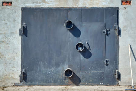 Metal garage door with round protections for padlocks. The wall of the garage is concrete and plastered. Top ventilation grilles. Rake for cleaning the area in front of the building.の写真素材