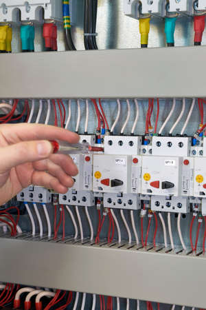 The worker checks and tests the operation of the electric Cabinet after its production. In the electrical Cabinet mounted circuit breakers motor protection. Industrial circuit breakers.の写真素材