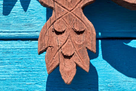 Wooden element of window frames on the old village house. Classical wood carving in Russia. The element in the form of a terrible moth. Trim on the background of the Board wall of the house.の写真素材