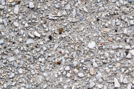 The surface of the concrete wall of the building is covered with a variety of different stones. The stones are small and large, white and brown. Exterior wall design. Background, backdrop, texture.の写真素材