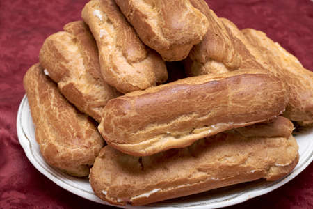 Some sweet and delicious eclairs are heaped on the plate. Homemade eclairs with custard, cooked with your own hands. Cakes cut in half. Inside filled with sweet cream. Delicious dessert.の写真素材