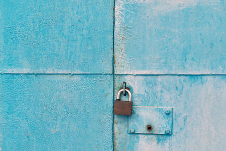 The blue iron gate is closed with a padlock. On one door there is a round hole for the key of the hidden internal lock. The metal sheets of the doors are divided into four parts. Background, backdrop.の写真素材
