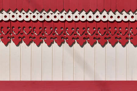 The surface of the wall or fence decorated with carved wooden boards patterns and painted red and beige paint. Patterns in the form of holes, corners and various bends. Simple, beautiful decoration.の写真素材