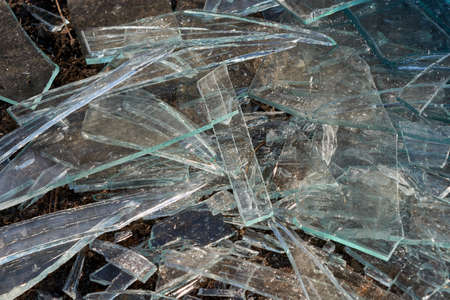 A pile of different sharp pieces of broken glass lying on the ground. Pieces of glass of different size and shape. Many pieces of oblong shape. The sharp edges glisten in the sunlight.の写真素材