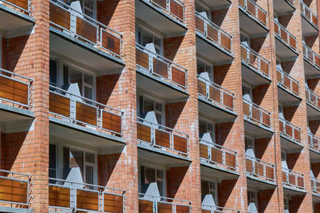 The facade of a brick building with several rows of balconies or loggias. Loggias with fences of three rectangular sheets of plexi glass.の写真素材