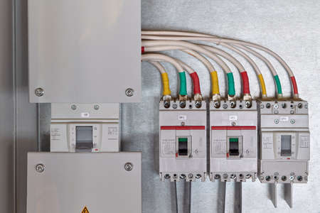 A large input circuit breaker and a series of circuit breakers with cables connected to them. Each phase of a wire or cable is color-coded. Electricity distribution. High current circuit breakers.の写真素材