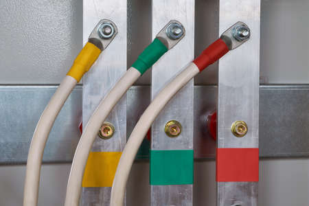 Three electric cable is connected to the vertical aluminum busbars in the electrical control panel by means of bolted connectors. Cables and busbars are color-coded. Electricity distribution.の写真素材