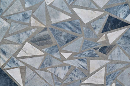 The surface of the wall or floor is made of triangular pieces of marble or granite. Triangular tiles of different sizes and colors are arranged in a chaotic order. Background or backdrop.の写真素材