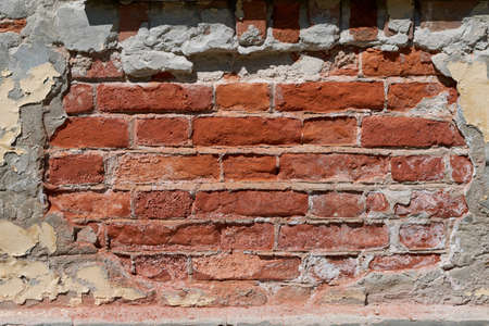The brick wall of an old building with fallen plaster. Damaged by weather and time part of the wall of red brick. A space was formed with an oval frame with uneven edges. Background or backdrop.の写真素材