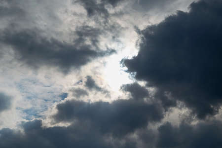 Storm clouds are coming and obscuring the sun. Bad weather. Strong wind and feeling the rain. The clouds are dark blue. The clouds are lit by sunlight.の写真素材