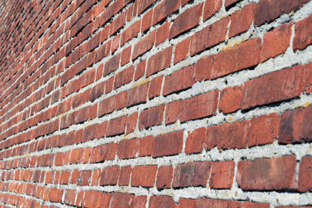 Large red brick wall. Side view. Perspective. The surface of the wall is slightly curved. Brickwork of a large number of bricks. Seams from a thick layer of cement mortar.の写真素材