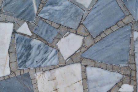The surface is tiled with rectangular and triangular mosaic tiles of various sizes. The polygons are arranged in a chaotic order. Between tiles joints in concrete. Background, texture, backdrop.の写真素材