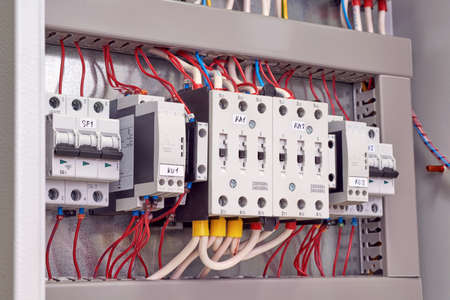 Two power electrical contactors, phase control relays and circuit breakers in the electrical Cabinet. Wires are connected to starters, relays and switches. Manufacture, repair, adjustment, automation.の写真素材