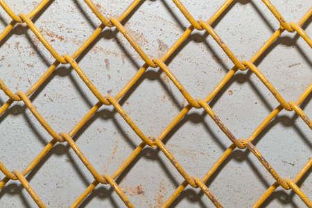 Metal grid in the form of squares or rhombuses on the wall made of iron sheet. Double fence. The mesh wire is painted yellow. The metal sheet is grey with traces of rust.の写真素材