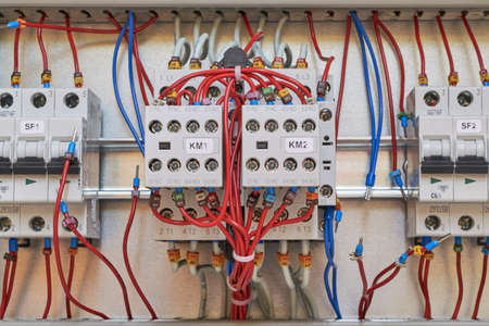 A bundle of red wires connected to two additional contacts of electrical contactors or magnetic starters. Two automatic switches are visible on the sides. Assembly and repair of electrical cabinets.の写真素材